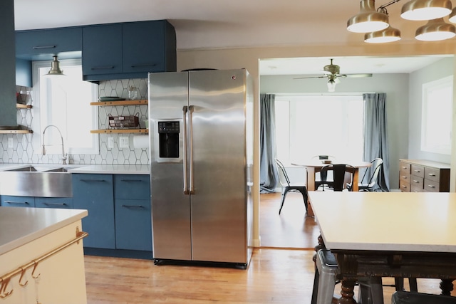 kitchen featuring open shelves, decorative backsplash, stainless steel refrigerator with ice dispenser, blue cabinetry, and light wood-style floors