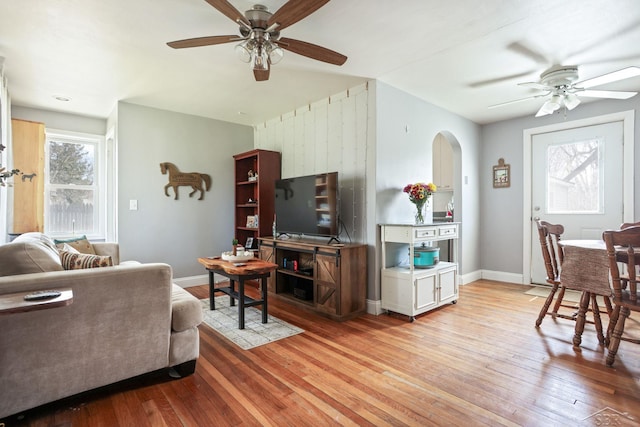 living area featuring a ceiling fan, baseboards, arched walkways, and wood-type flooring