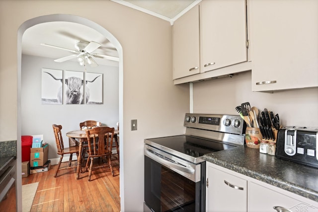 kitchen featuring crown molding, light wood-style flooring, stainless steel range with electric cooktop, arched walkways, and a ceiling fan