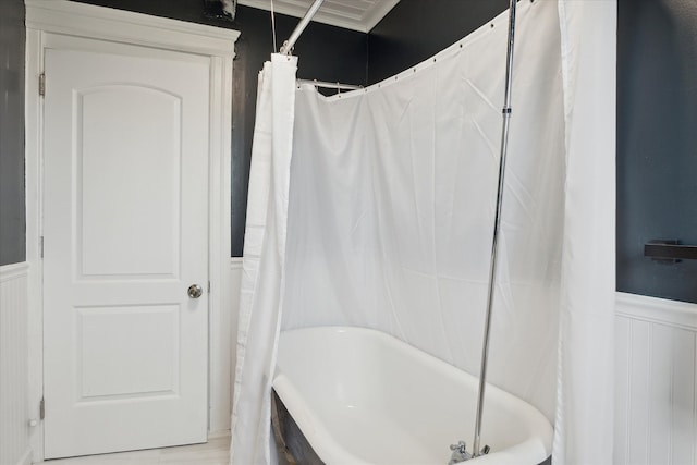 bathroom featuring a decorative wall, a shower with curtain, a tub to relax in, and a wainscoted wall
