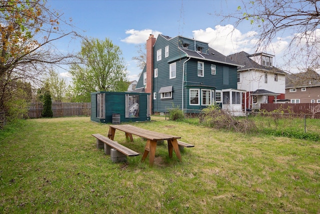 back of house with a lawn, fence, an outbuilding, and a chimney