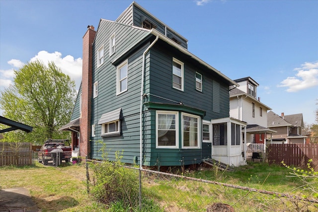 rear view of house with fence, a chimney, and a sunroom