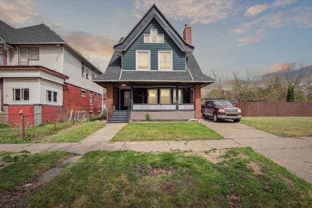 view of front of home with a shingled roof, a front lawn, covered porch, and a chimney