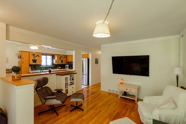 living room featuring crown molding, light wood-type flooring, and visible vents