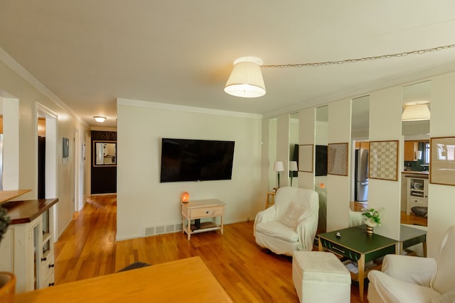 living area featuring crown molding, baseboards, visible vents, and wood finished floors