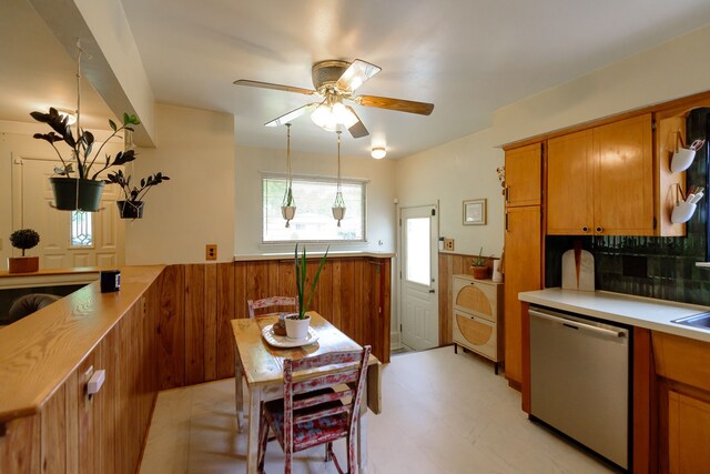kitchen with brown cabinetry, wainscoting, ceiling fan, and dishwasher