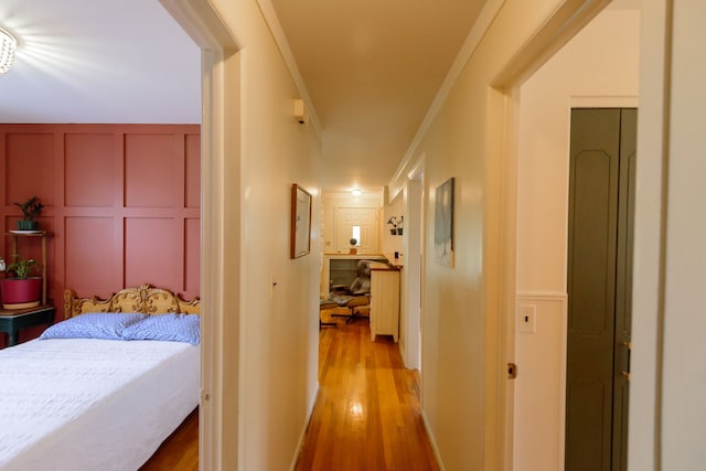 hall with light wood-style floors, ornamental molding, and a decorative wall