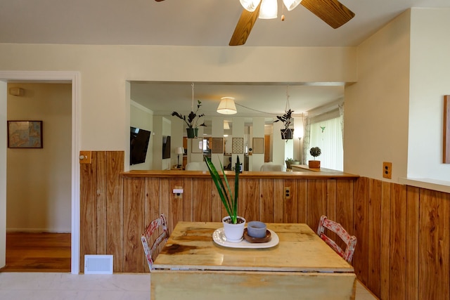 dining area with wooden walls, ceiling fan, and visible vents