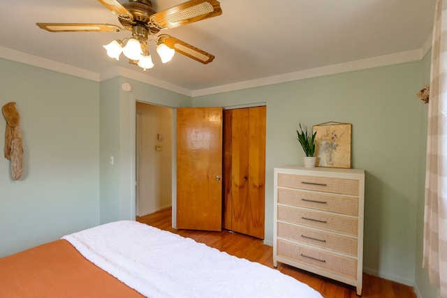 bedroom with crown molding, ceiling fan, wood finished floors, and a closet
