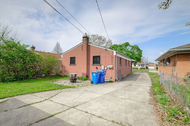 view of home's exterior with fence, a chimney, driveway, and brick siding