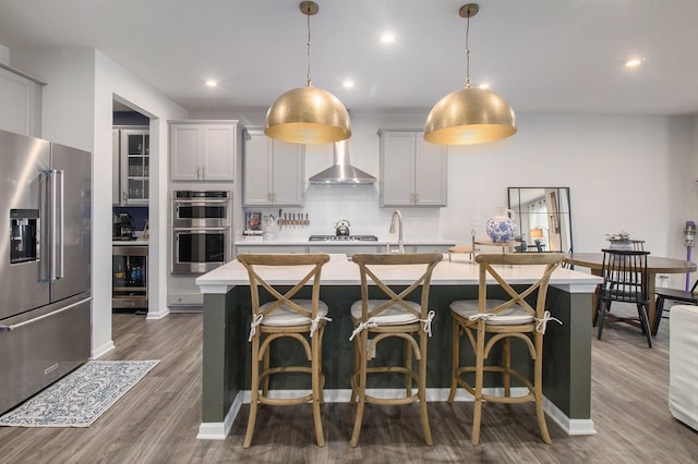 2670 Ironton Dr, Commerce Twp, MI 48382 - kitchen featuring a center island with sink, wall chimney range hood, light countertops, appliances with stainless steel finishes, and beverage cooler