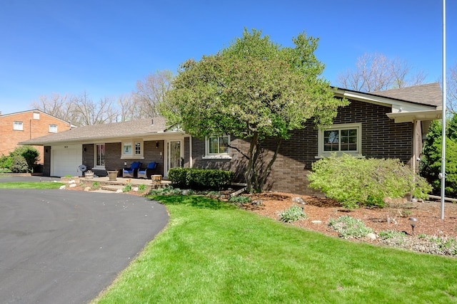 ranch-style home with brick siding, an attached garage, a front yard, and aphalt driveway