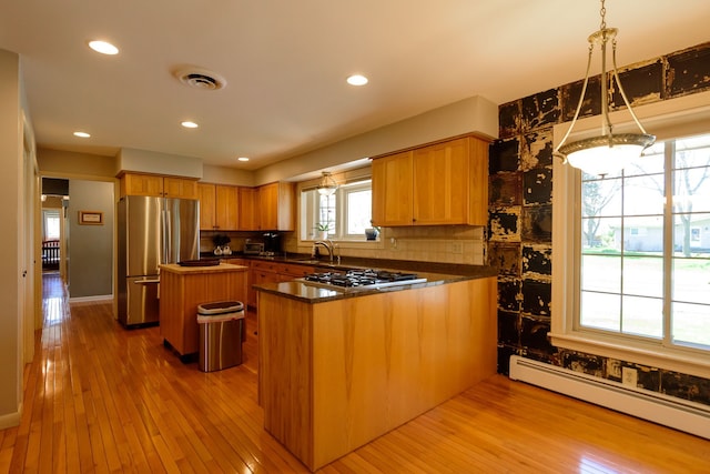 kitchen with dark countertops, baseboard heating, a center island, hardwood / wood-style flooring, and appliances with stainless steel finishes