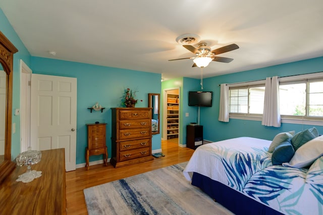 bedroom with a closet, wood finished floors, baseboards, a walk in closet, and ceiling fan