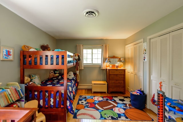 bedroom with visible vents, a baseboard radiator, multiple closets, and wood finished floors