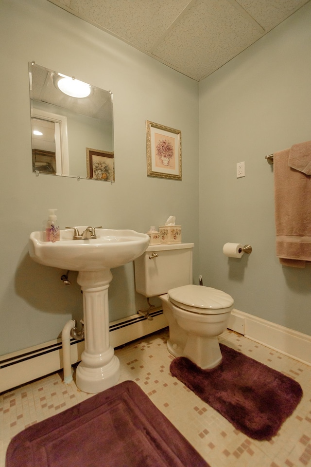 half bath featuring baseboards, a drop ceiling, a baseboard heating unit, and toilet