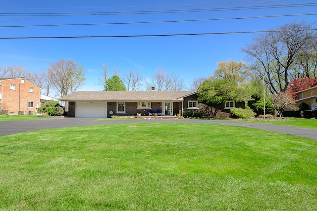 ranch-style home with a garage, a chimney, a front yard, and aphalt driveway