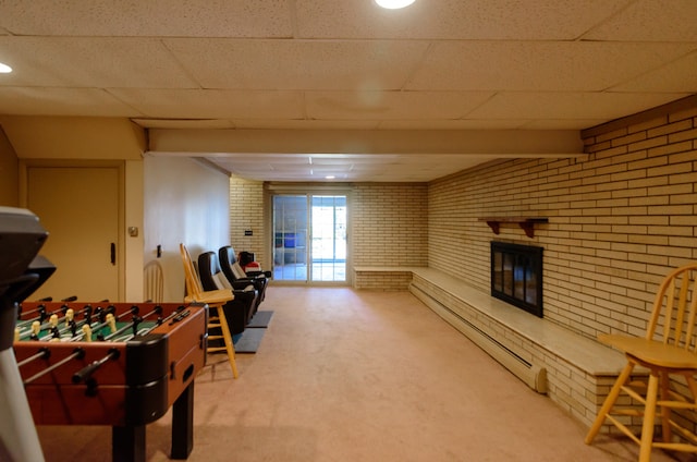 recreation room featuring carpet floors, brick wall, a paneled ceiling, and a fireplace