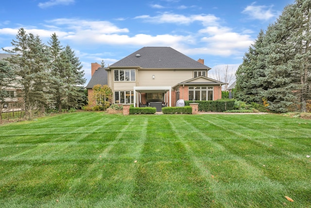 back of house featuring a chimney, a jacuzzi, a yard, brick siding, and a sunroom