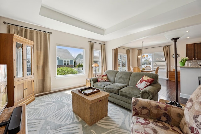 living area featuring an inviting chandelier, a raised ceiling, wood finished floors, and a healthy amount of sunlight