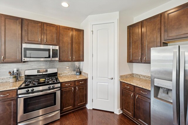 kitchen featuring dark brown cabinetry, appliances with stainless steel finishes, tasteful backsplash, light stone countertops, and dark wood-type flooring