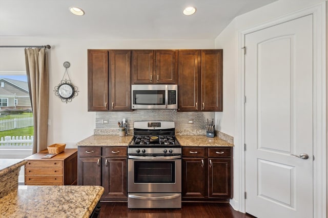 kitchen featuring dark brown cabinetry, light stone countertops, tasteful backsplash, dark wood finished floors, and appliances with stainless steel finishes