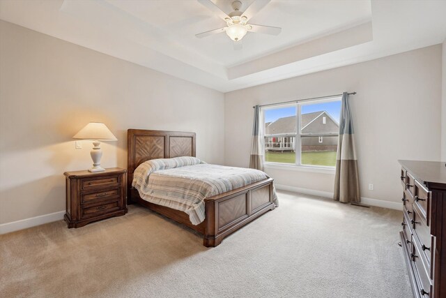 bedroom with baseboards, light colored carpet, and a tray ceiling