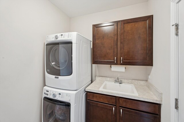 clothes washing area featuring a sink, cabinet space, and stacked washer / dryer