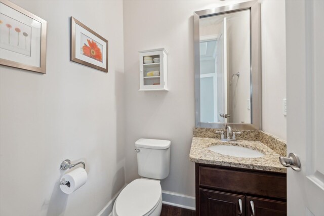half bathroom with baseboards, wood finished floors, toilet, and vanity