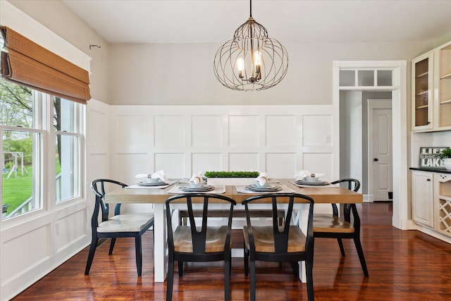 dining space featuring dark wood-style flooring, a decorative wall, and a notable chandelier
