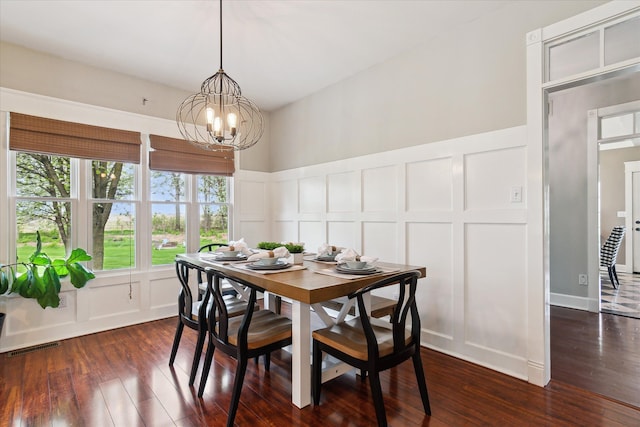 dining space with wainscoting, a decorative wall, dark wood finished floors, and a chandelier