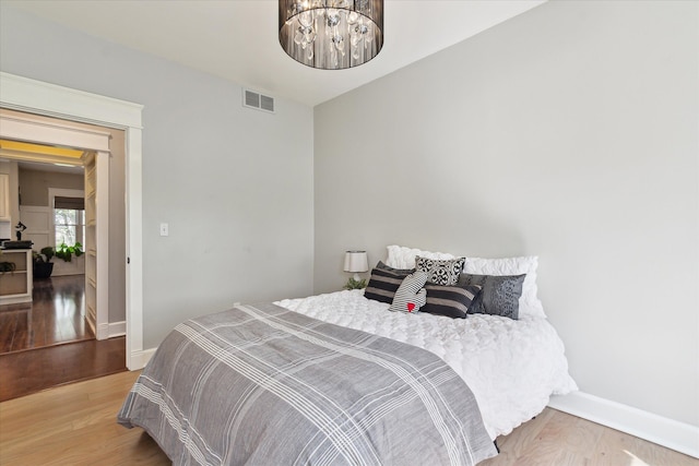 bedroom with baseboards, visible vents, and wood finished floors