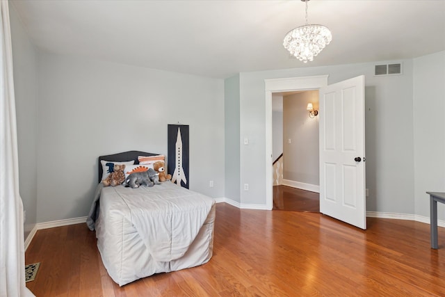 bedroom with visible vents, baseboards, wood finished floors, and a notable chandelier