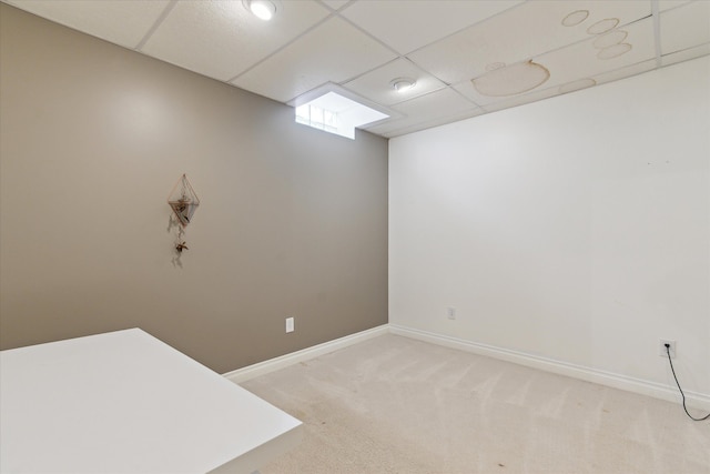 interior space featuring baseboards, a drop ceiling, and light carpet