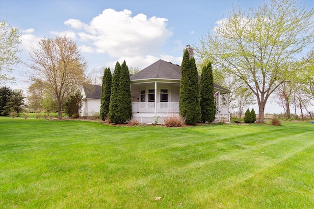 view of side of home with a chimney, a yard, and a porch