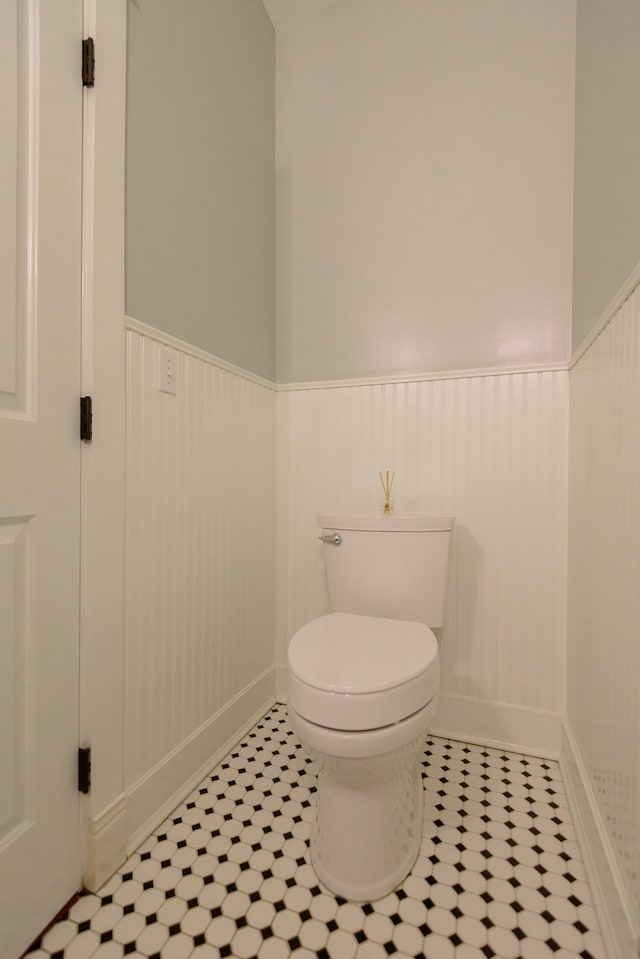 bathroom featuring baseboards, wainscoting, tile patterned floors, and toilet