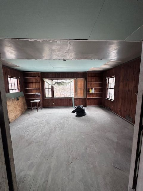 unfurnished living room featuring wooden walls, plenty of natural light, and unfinished concrete flooring