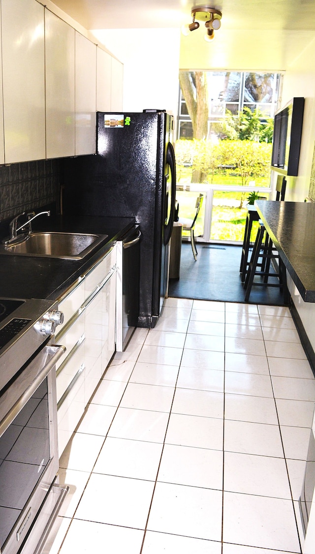 kitchen with dark countertops, tasteful backsplash, light tile patterned floors, a sink, and oven
