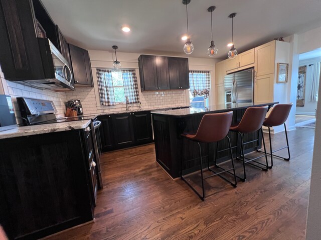 kitchen featuring a breakfast bar area, backsplash, dark wood-style flooring, appliances with stainless steel finishes, and a center island