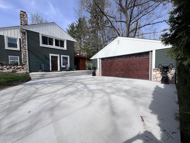 view of side of property with an outdoor structure, a garage, stone siding, a chimney, and board and batten siding