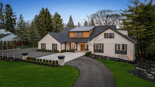 modern farmhouse style home featuring a standing seam roof, covered porch, a chimney, and a front lawn