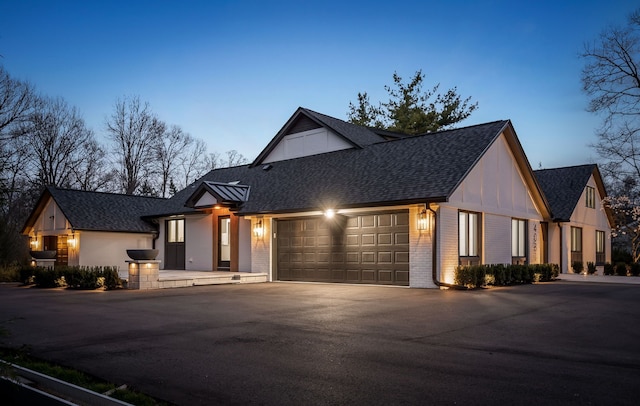 modern farmhouse with brick siding, a garage, roof with shingles, and driveway