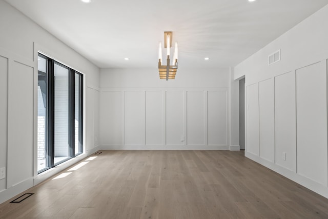 interior space with an inviting chandelier, light wood finished floors, a decorative wall, and visible vents