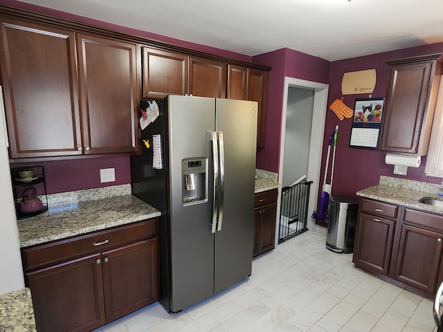 kitchen featuring stainless steel fridge with ice dispenser, light stone counters, a sink, and dark brown cabinets