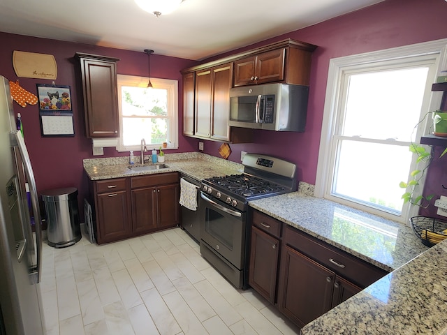 kitchen featuring appliances with stainless steel finishes, a sink, pendant lighting, and light stone counters