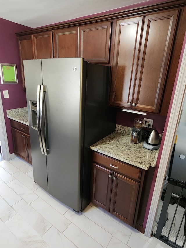 kitchen with stainless steel fridge with ice dispenser, light marble finish floors, and light stone counters