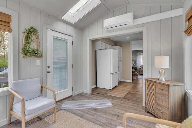 sitting room featuring baseboards, an AC wall unit, vaulted ceiling with skylight, and light wood-style floors