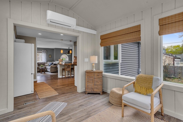 living area featuring wood finished floors, plenty of natural light, an AC wall unit, and vaulted ceiling