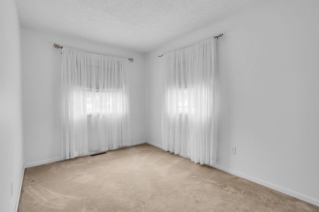 empty room with a textured ceiling, visible vents, a healthy amount of sunlight, and carpet flooring