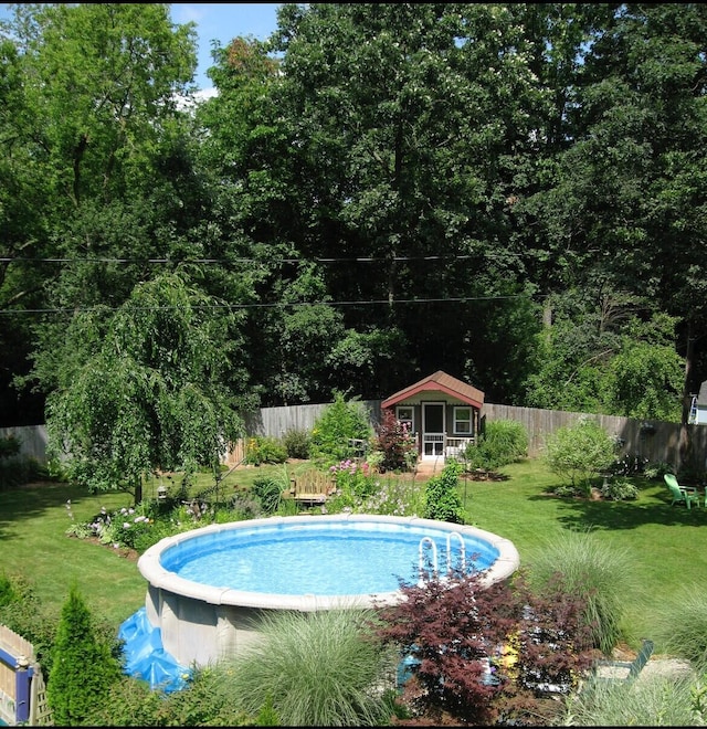 view of swimming pool featuring an outdoor structure, a fenced in pool, a yard, and a fenced backyard